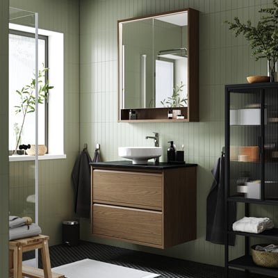 Modern bathroom setup: ÄNGSJÖN cabinet in brown oak, central round basin, mirror, plants, towels, minimalist style.