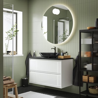 Modern ÄNGSJÖN bathroom: white cabinet, round mirror, dark basin; wall-mounted with green-tiled walls and black fixtures.