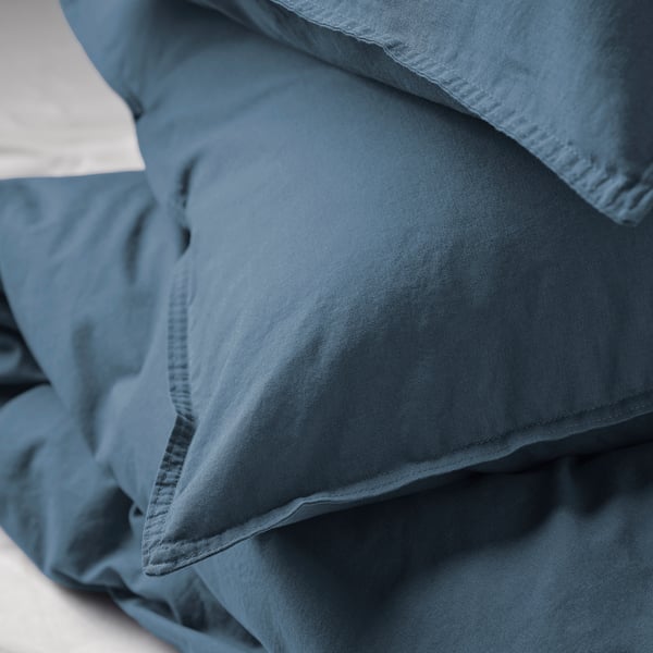 A close-up of a stack of soft, blue-gray duvet covers, showcasing high-quality cotton fabric and precise stitching.