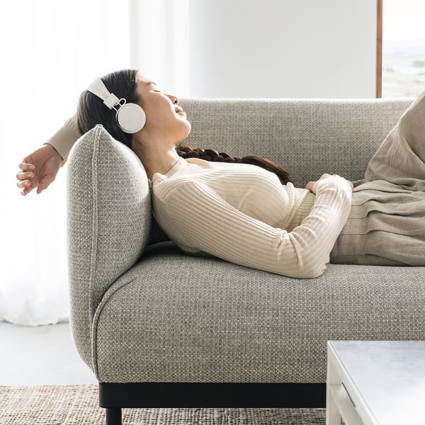 Woman relaxes on modern gray ÄPPLARYD sofa, listening to headphones.