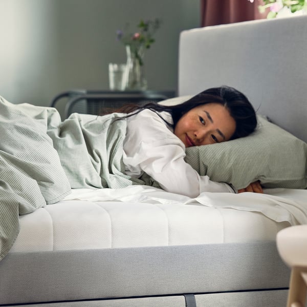 Woman sleeping on white mattress with pillow. Softly lit room, glass table with vase.
