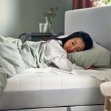Woman sleeping on white mattress with pillow. Softly lit room, glass table with vase.