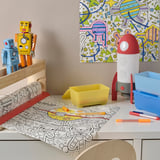 Childrens desk with AFTONSPARV led lamp, robot toys, coloring mat, and pens. The lamp changes colors, promoting a fun and creative environment.