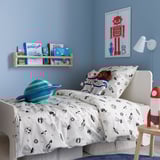 Cozy kids space-themed bedroom with astronaut bedding, plush toys, books, and robot art.