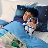 Boy lay on blue bedding holding astronaut teddy bear, smiling happily.