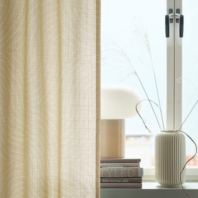 ÅKERMOLKE curtains, beige, textured, hang near a window, next to a tall vase and stacked books.