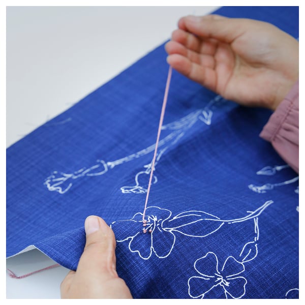 Person hand-embroidering blue cushion cover with white floral design. Thread is visible as they work on intricate stitching.