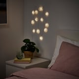Cozy bedroom with soft AKTERPORT lights, peach pillows, plant, books, and nightstand.