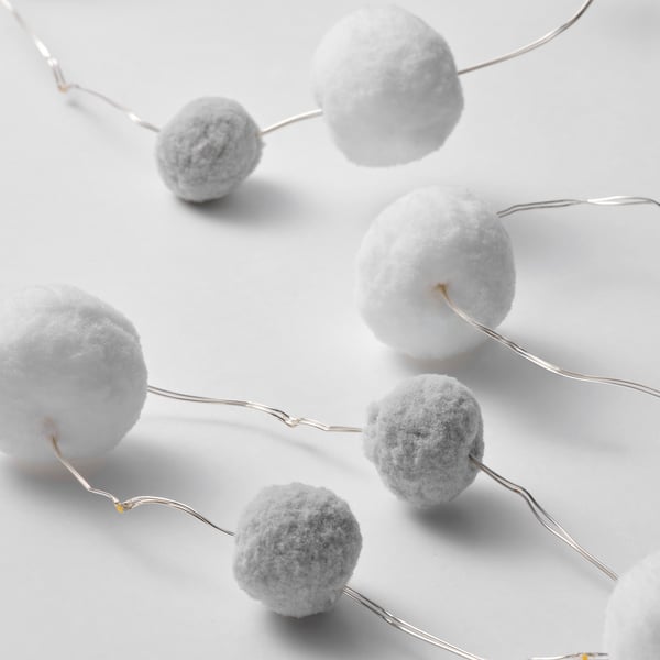 Image shows a close-up of decorative string lights featuring several round, fuzzy pom-pom bulbs connected by thin wires.