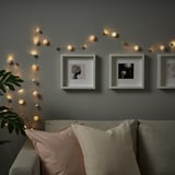 Modern living room with fairy lights above couch, three framed photos, cozy pillows, and a green plant.