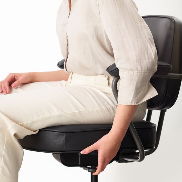 Person adjusting ergonomic office chairs armrest. Chair has padded arms and lumbar support.