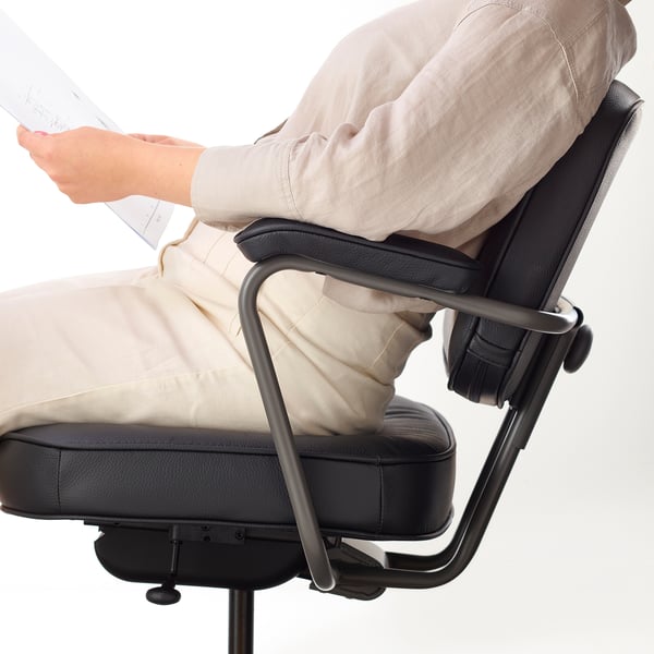 Person sitting in ergonomic office chair. Chair has padded armrests and back support. Hands hold papers.
