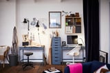 Modern home office with ALEX drawers, desk, wicker chair, artwork, lamps, mirror, dark curtains, wooden floor.