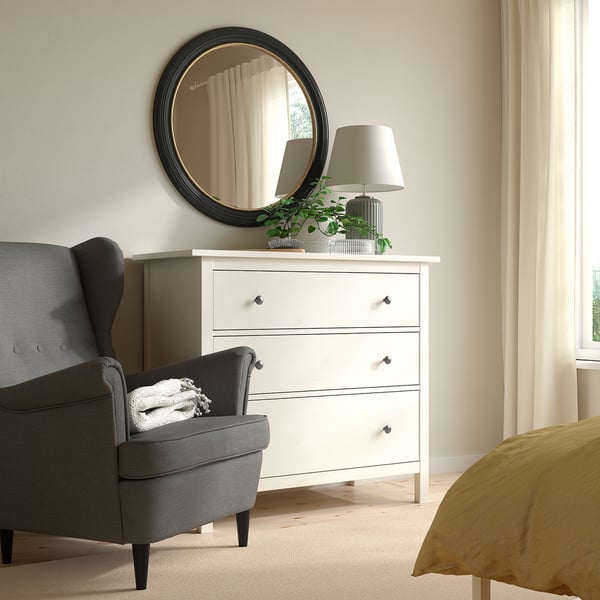Cozy bedroom with ALMARÖD round black mirror, white chest of drawers, gray chair, and yellow bedding. Mirrors thin gold edge adds style.
