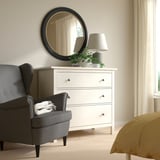 Cozy bedroom with ALMARÖD round black mirror, white chest of drawers, gray chair, and yellow bedding. Mirrors thin gold edge adds style.