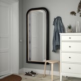 Black-framed ALMARÖD mirror with gold trim next to white dresser and denim jacket.