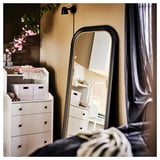 Bedroom with ALMARÖD black mirror, linen curtains, white dresser, pink flowers, and black wall lamp.