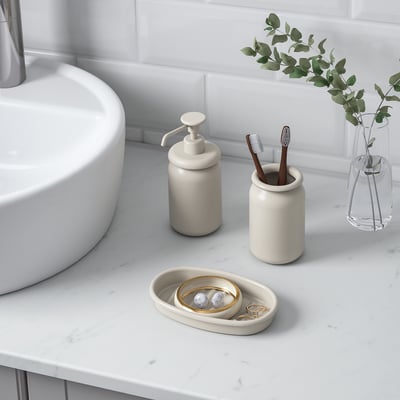 A beige ÅLTJÄRN bathroom set. It includes a soap dispenser and a toothbrush holder, both with rounded edges, placed in a matching tray.