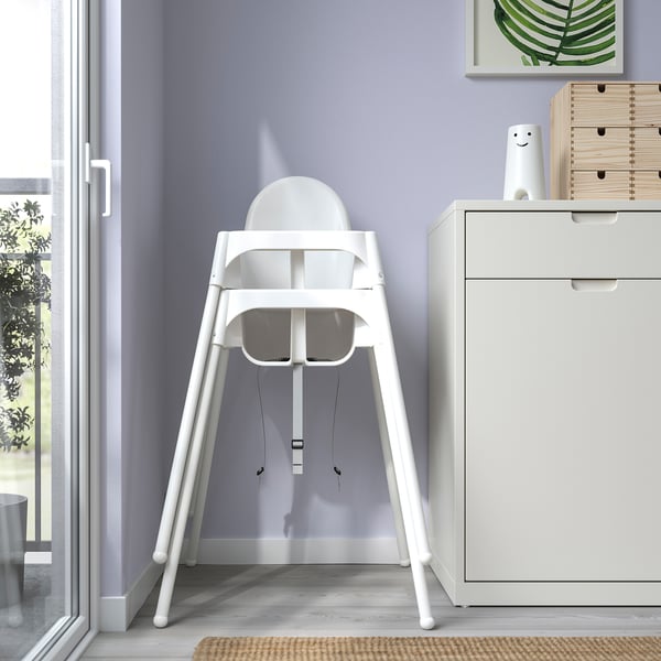 White highchair against purple wall, easy to assemble/disassemble. Safety belt included.