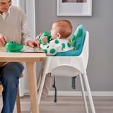Baby in ANTILOP highchair eats from frog bowl as woman assists.