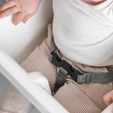 Child in anti-lope highchair, secured with safety belt. Belt is adjusted by adult hand.