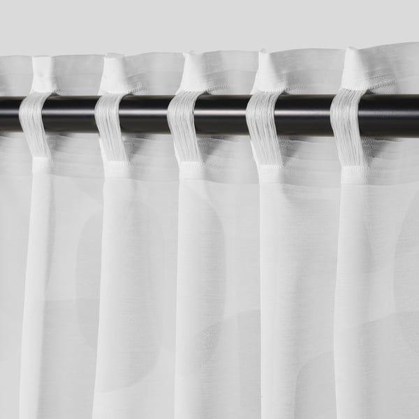 White curtains with geometric pattern hanging from black rod, allowing light through, offering privacy.