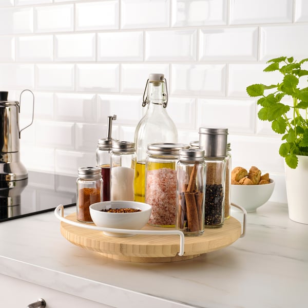 Bamboo lazy susan with glass jars of spices and herbs on kitchen counter.