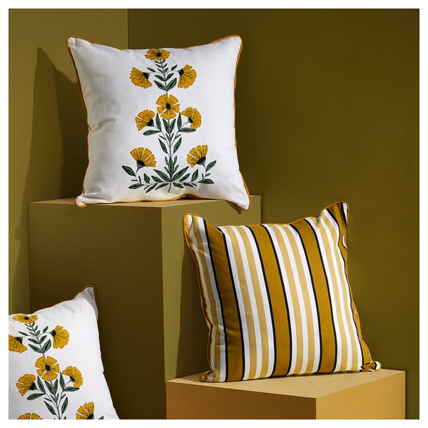 Three square throw pillows displayed on stands; two with yellow floral patterns, one with yellow, white, black stripes.
