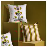 Three square throw pillows displayed on stands; two with yellow floral patterns, one with yellow, white, black stripes.