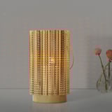 Golden AROMATISK lantern, wave-shaped, metal, sits on table, smaller than vase, lit candle.