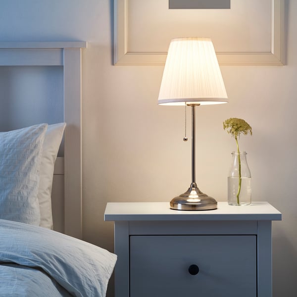 ÅRSTID lamp on bedside table, white shade, metallic base.