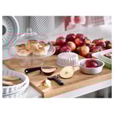 Kitchen display with apples, pastries, cutting board, peelers, bowls; clear glass dome lid.