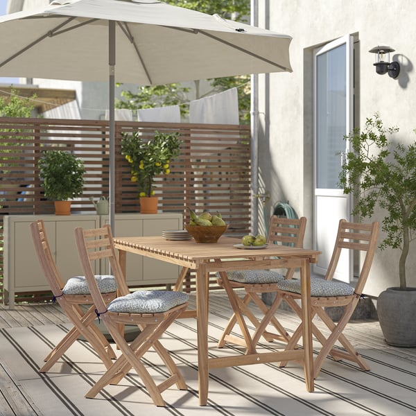 Wooden outdoor dining set with light table, gray cushioned chairs, plants, and umbrella.