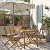 Cozy wooden patio set with 4 cushioned chairs. Compact, fits small patio. Light wood contrasts with plants and walls. Umbrella offers shade.