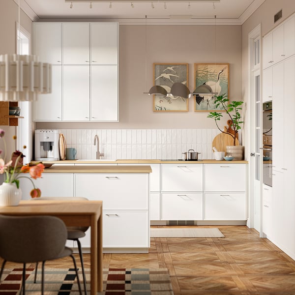 Modern kitchen with white ASPUDDEN cabinets, thin frames, and wood counters. Art and flowers decorate.