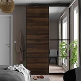 Bedroom with large sliding wardrobe doors: one mirrored, one wooden, reflecting room with plants.