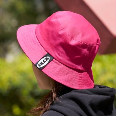 Woman wearing bright pink ikea bucket hat outdoors, shielding her face from the sun.