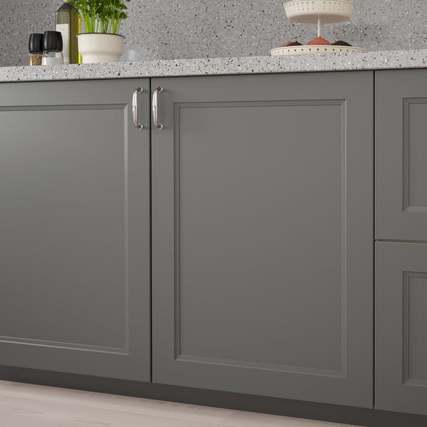 Dark grey kitchen cabinets with a sleek, modern design. Handles are on the left side, and theres a countertop with items like a plant and bowls on it.