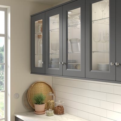 Grey AXSTAD cabinet with glass doors displays dishes by window. Tall, fits above tiled counter.