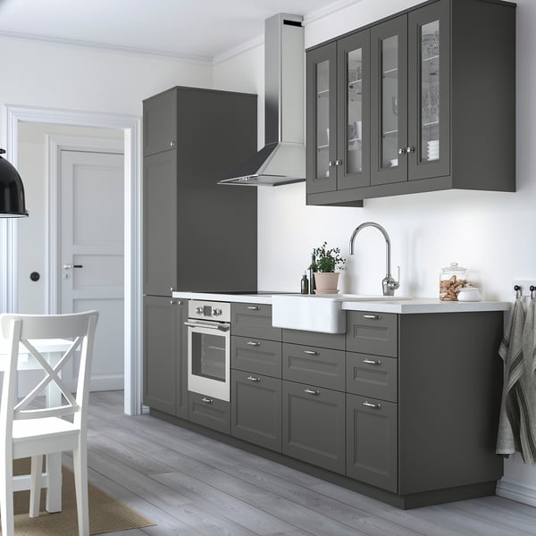 Modern kitchen with dark grey AXSTAD cabinets, some with glass doors, stainless steel appliances, white marble countertop, and white wooden chair.