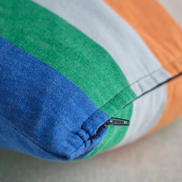 Close-up of multicolored striped cushion cover, showcasing zipper detail. Bright, modern design with blue, green, gray, and orange stripes.