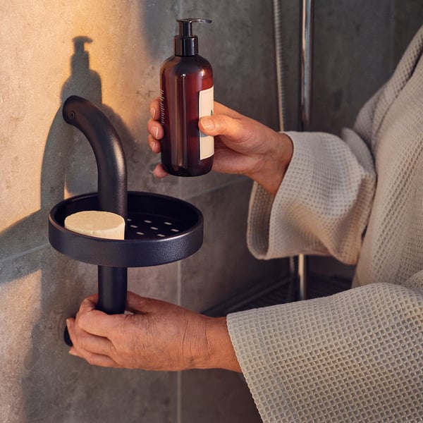 Person in gray robe holds dark gray shower caddy with soap.