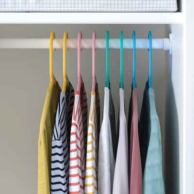 A colorful line of kids hangers, made of flexible plastic, holding various striped shirts.