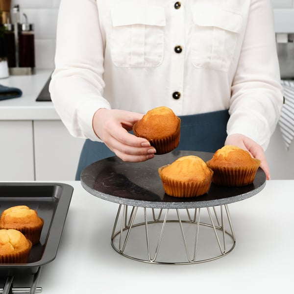 Person arranging muffins on round wire cake stand with rotating marble top on counter.