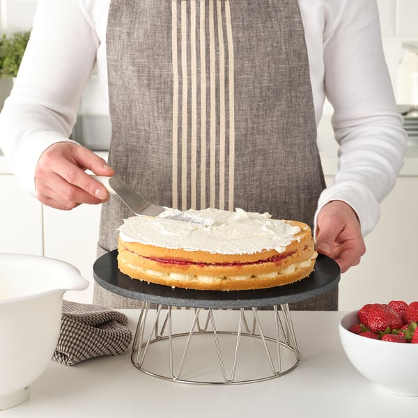 A person ices a cake on a rotating marble BAKGLAD stand, ensuring even coverage.