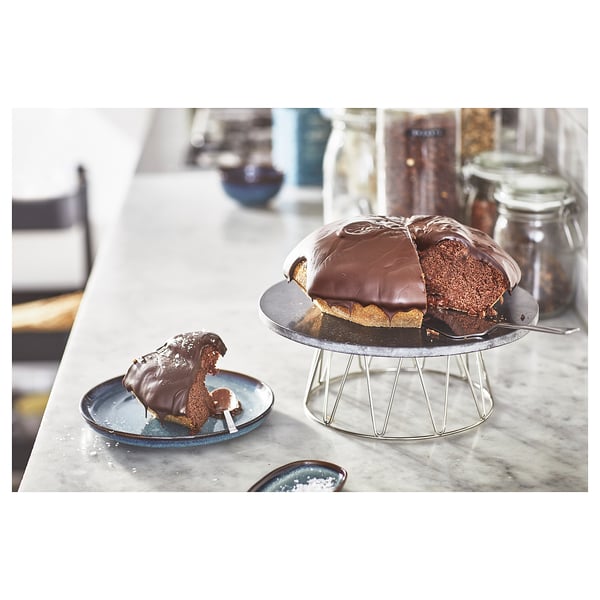Chocolate cake on silver rotating stand, with slice on blue plate. Kitchen counter background.