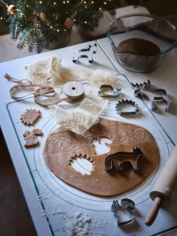 Baking scene with gingerbread dough on BAKTRADITION silicone mat, cookie cutters, ribbons, and a christmas tree.
