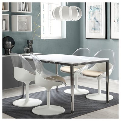 Modern dining area with white BALTSAR chairs and glass table on patterned rug, blue wall, shelves, and art.