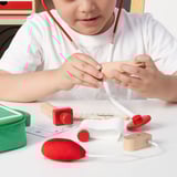 Child playing with doctor kit. Includes stethoscope, syringe, and toy medical tools. Promotes imagination, empathy, and motor skills.