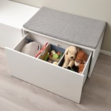 White toy box with grey dotted cushion. Stores plush toys, books, and stuffed animals. Foldable for space-saving.